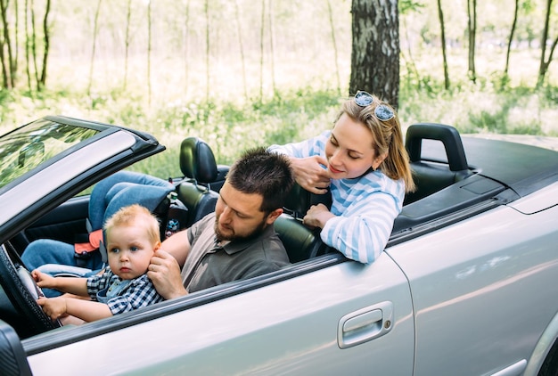 Foto mãe, pai e filhozinho num carro descapotavel, viagem familiar de verão à natureza.