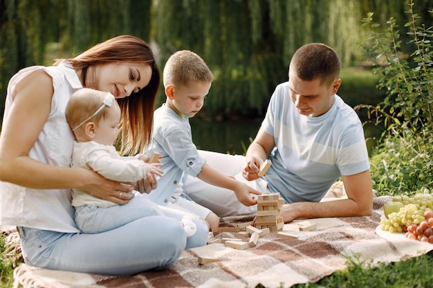 Mãe, pai, filho mais velho e filha pequena sentada em uma esteira de piquenique no parque. Família vestindo roupas brancas e azuis claras