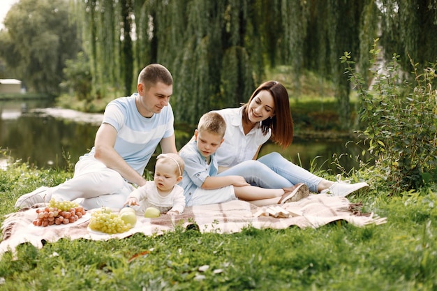 Mãe, pai, filho mais velho e filha pequena sentada em uma esteira de piquenique no parque. Família vestindo roupas brancas e azuis claras