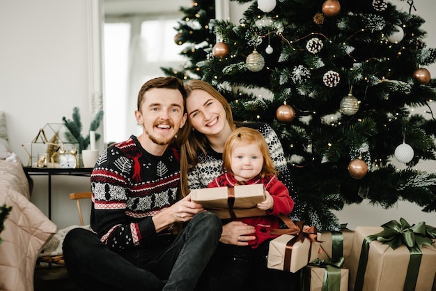 Mãe pai trocando presentes com a filha Pais e criança se divertindo perto da árvore de Natal dentro de casa Amando a família com presentes no quarto Na manhã anterior ao Natal Retrato de perto