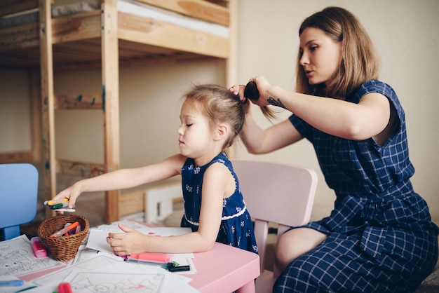 Mãe penteia a filha e arruma o cabelo.