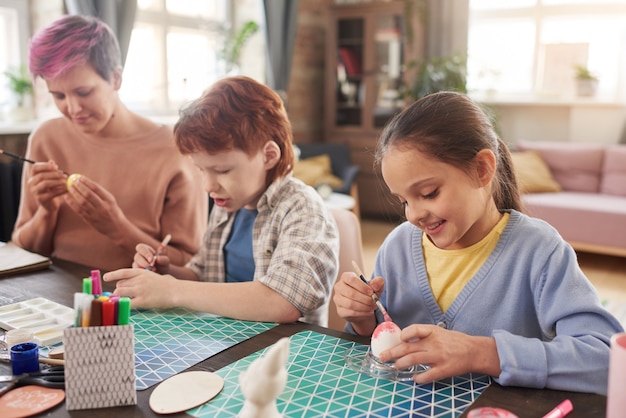 Mãe pintando ovos para a Páscoa junto com seus filhos na mesa em casa