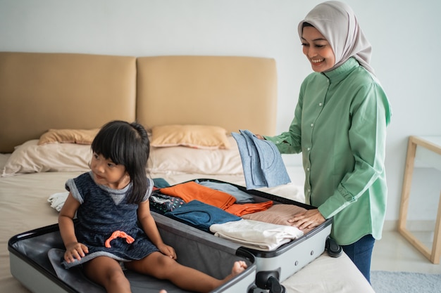 Mãe prepara roupas e sua filha brinca com sua mala