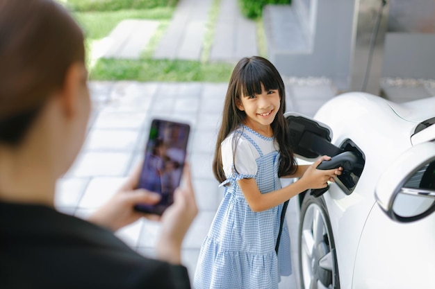 Mãe progressiva tirando uma foto da filha recarregando o carro EV em casa