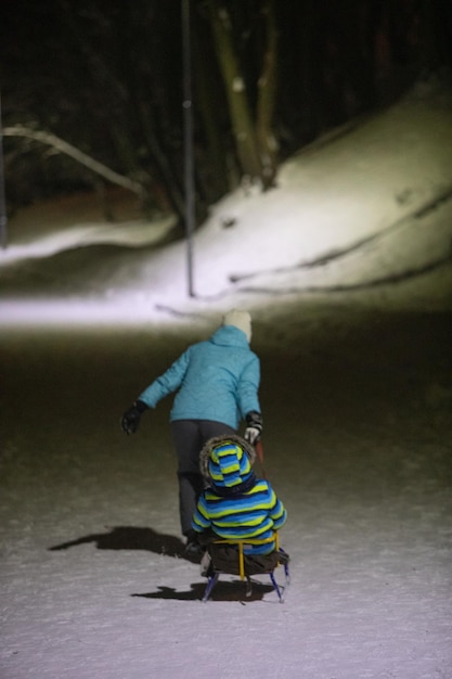 Mãe puxando trenó com criança pelo parque da cidade de inverno