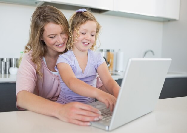 Foto mãe que ajuda a filha a usar o laptop na mesa