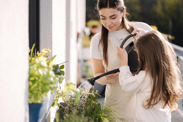 Mãe regando planta com sua adorável filha feliz jardinagem familiar na varanda