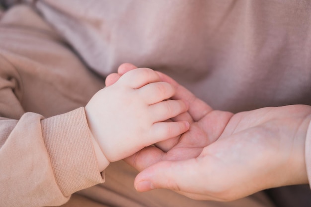 Foto mãe segura a mão do bebê em roupas bege