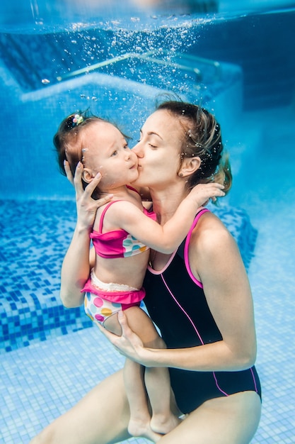 Mãe segura filha estão imersos na água, nadando debaixo d'água na piscina infantil. mergulhando bebê. aprender criança infantil a nadar. jovem mãe ou instrutor de natação e uma menina feliz.