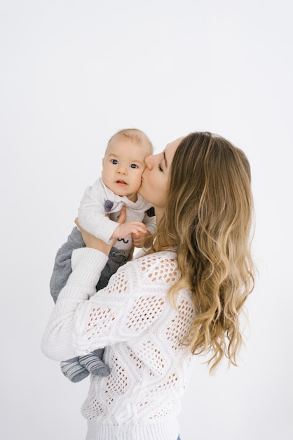 Mãe segura o filho de cinco meses nos braços contra uma parede leve e o beija na bochecha