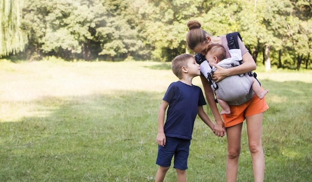 Mãe segura o filho mais velho pela mão e usa o mais novo em uma tipoia