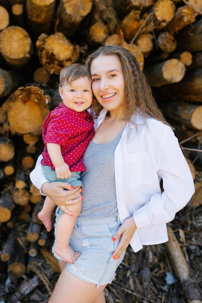 Foto mãe segura seu bebê em seus braços contra o fundo de troncos de madeira ao ar livre na floresta