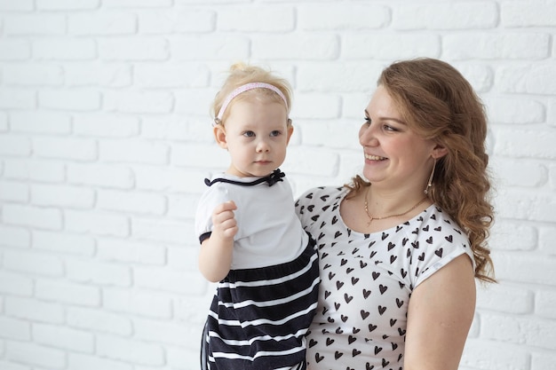 Mãe segura seu filho com aparelhos auditivos e implantes cocleares na parede de tijolos brancos com espaço de cópia
