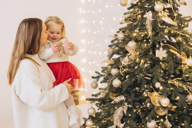 Mãe segurando filha decorando árvore de Natal com ornamentos dourados