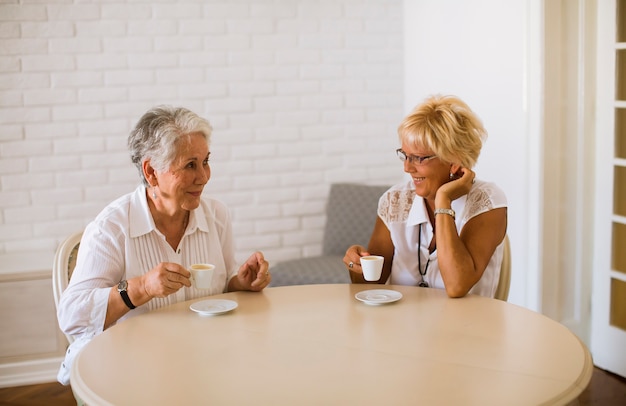 Foto mãe sênior e filha velha madura, conversando e tomando café no quarto