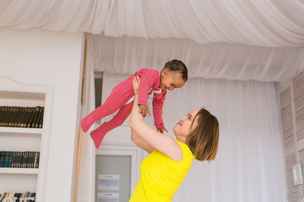 Mãe sorridente brincando com o filho bebê de raça mista em casa.