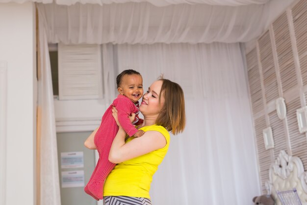 Mãe sorridente brincando com o filho bebê de raça mista em casa.