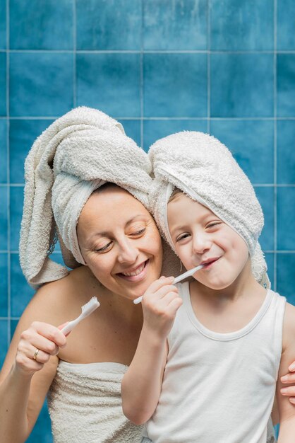 Foto mãe sorridente com filho escovando os dentes enquanto está de pé contra a parede