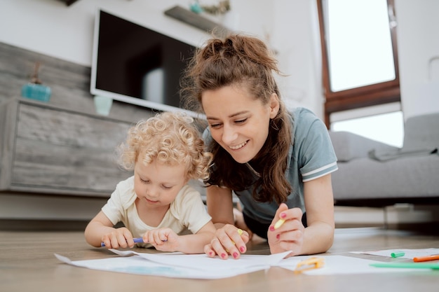 Mãe sorridente com sua filha pré-escolar passando seu tempo livre desenhando juntos