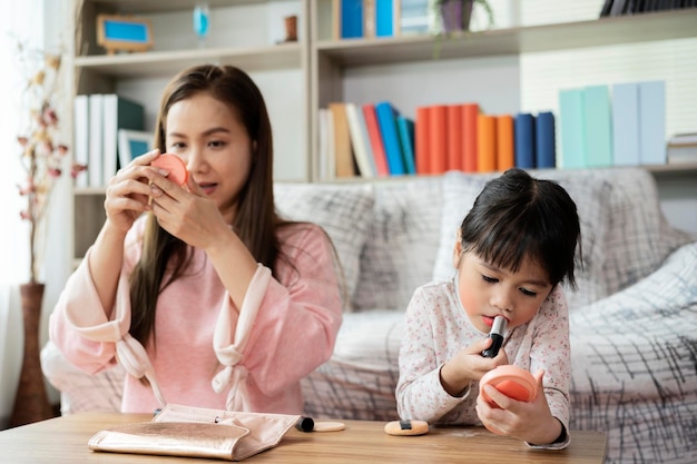 Mãe sorridente e filha pré-escolar fazendo maquiagem juntos