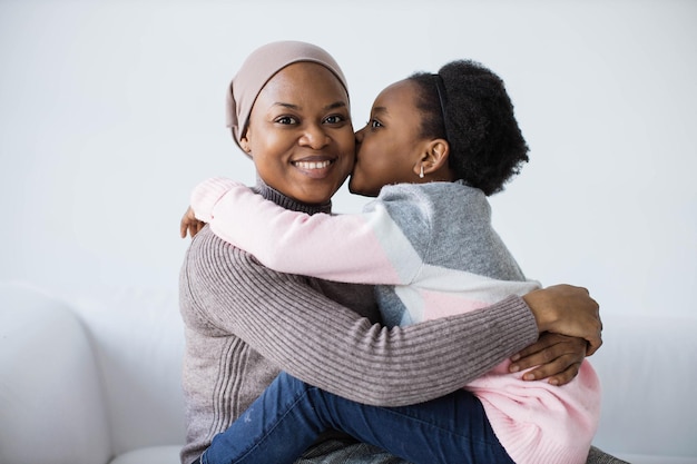 Mãe sorrindo para a câmera enquanto a filha a beija