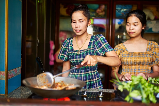 Mãe tailandesa cozinhando com filha adolescente em cozinha rústica