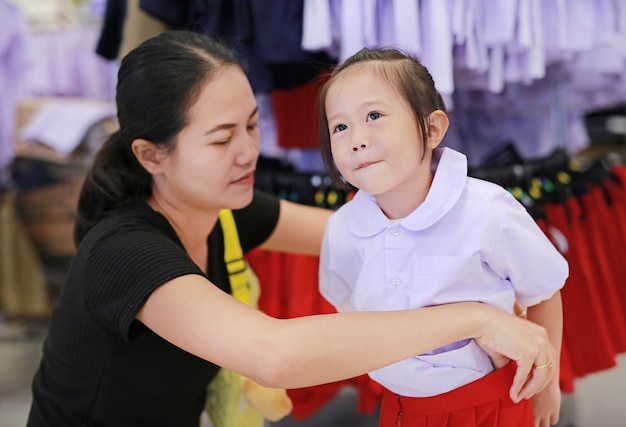 Mãe tenta vestir uniforme escolar para sua filha, crianças do jardim de infância.