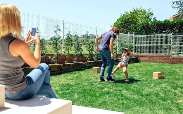 Mãe tirando foto móvel de seu marido e filho brincando no jardim