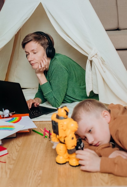 Mãe trabalha fones de ouvido laptop criança próximos jogos