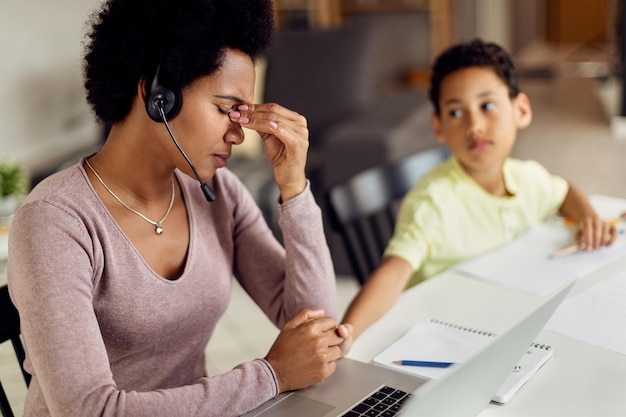 Foto mãe trabalhadora afro-americana com dor de cabeça enquanto trabalhava no laptop em casa