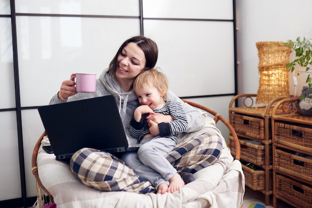 Mãe, trabalhando com o computador portátil em casa e brincando com seu bebê.