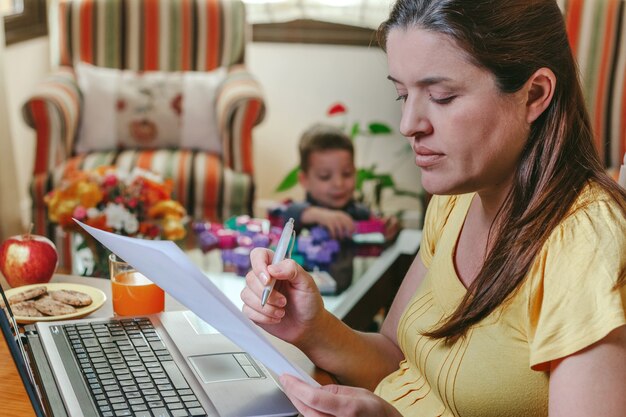 Mãe trabalhando no laptop na sala de estar enquanto o filho brinca