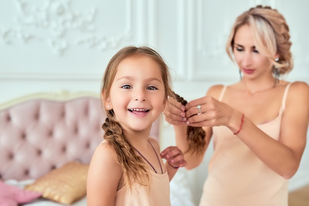 Mãe tranças tranças para fofa filha sorridente