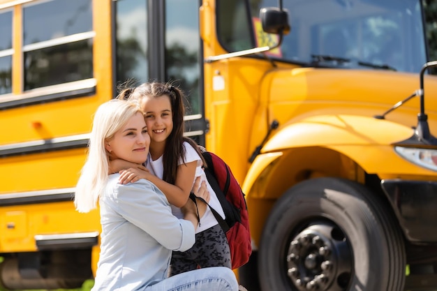 Foto mãe traz sua filha para a escola perto do ônibus escolar. de volta à escola