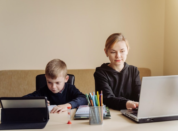 Mãe usando laptop e tablet ensinando com seu filho online em casa em seu quarto