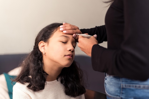 Mãe verifica a temperatura de sua filha em casa com o termômetro e examina sua testa