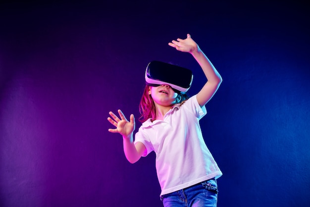 Mädchen 7 yo VR-Kopfhörerspiel auf buntem erfahren. Kind, das ein Spielgerät für virtuelle Realität verwendet.