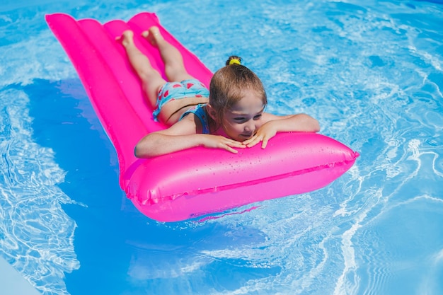 Mädchen 78 Jahre alt schwimmt im Pool auf einer aufblasbaren rosa Matratze Sommerferien