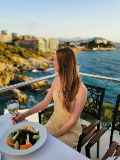 Mädchen am Meer in einem Restaurant bei einem romantischen Abendessen mit einem Glas Wein.
