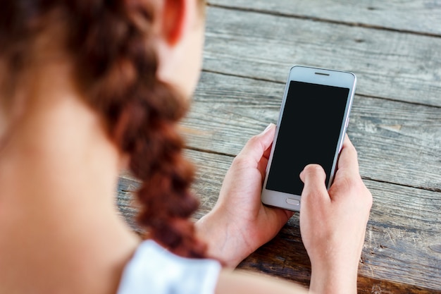 Mädchen an einem Holztisch, der ein Telefon in ihrer Hand hält