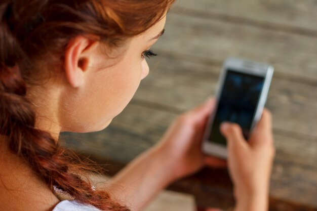 Mädchen an einem Holztisch, der ein Telefon in ihrer Hand hält