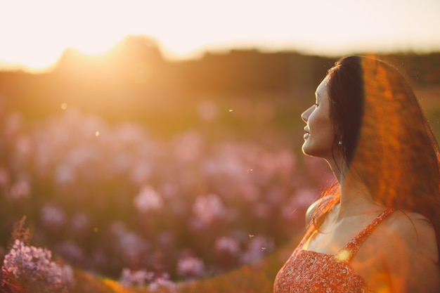 Mädchen auf blühendem Sally-Blumenfeld bei Sonnenuntergang. Lila Blumen und Frau. Weicher selektiver Fokus mit Sonneneruption.