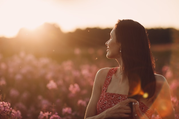 Mädchen auf blühendem Sally-Blumenfeld bei Sonnenuntergang. Lila Blumen und Frau.