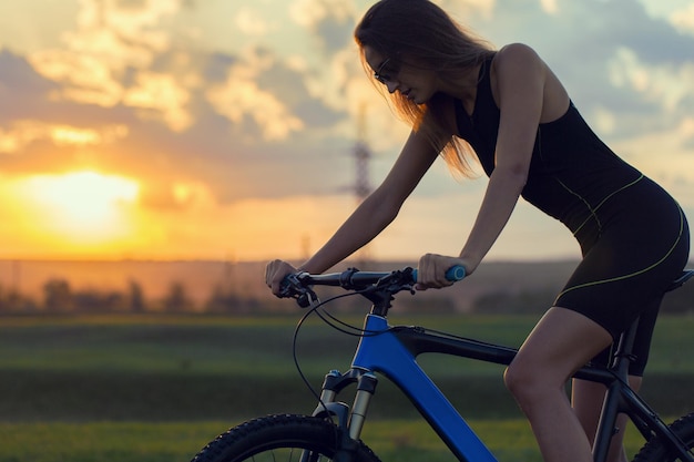 Mädchen auf einem Mountainbike im Gelände schönes Porträt eines Radfahrers bei Sonnenuntergang Fitness-Mädchen fährt auf einem modernen Kohlefaser-Mountainbike in Sportbekleidung Closeup Portrait eines Mädchens in einem Helm und Brille