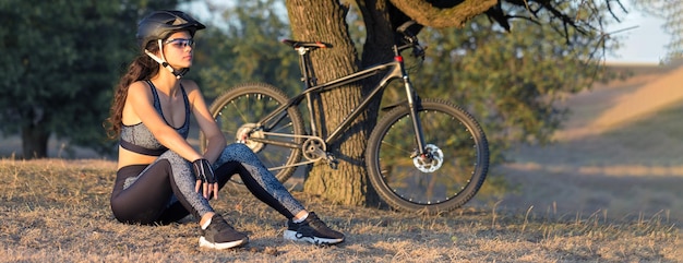 Mädchen auf einem Mountainbike im Gelände schönes Porträt eines Radfahrers bei Sonnenuntergang Fitness-Mädchen fährt auf einem modernen Kohlefaser-Mountainbike in Sportbekleidung Closeup Portrait eines Mädchens in einem Helm und Brille