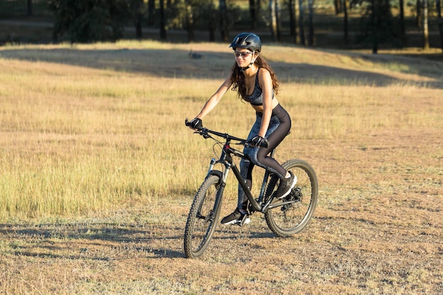 Mädchen auf einem Mountainbike im Gelände schönes Porträt eines Radfahrers bei Sonnenuntergang Fitness-Mädchen fährt auf einem modernen Kohlefaser-Mountainbike in Sportbekleidung Closeup Portrait eines Mädchens in einem Helm und Brille