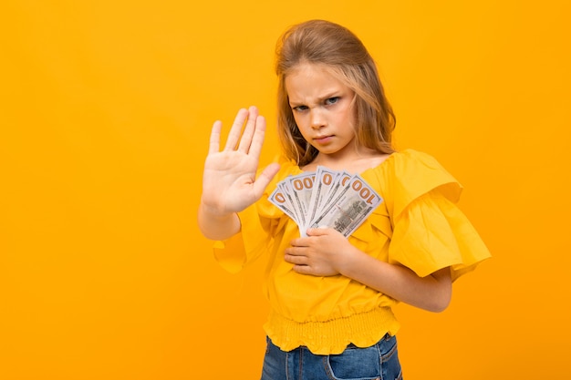 Mädchen auf gelbem Hintergrund hält wütend Geld in ihren Händen weigert sich zu teilen