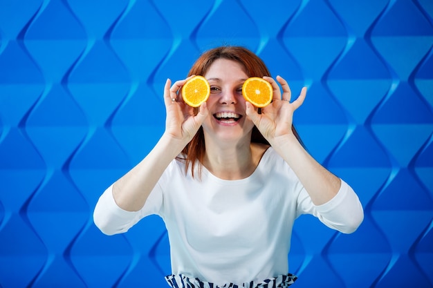 Foto mädchen auf hellblauem hintergrund in einer weißen bluse mit orangen in der hand