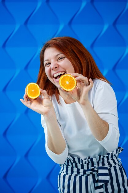 Mädchen auf hellblauem Hintergrund in einer weißen Bluse mit Orangen in der Hand