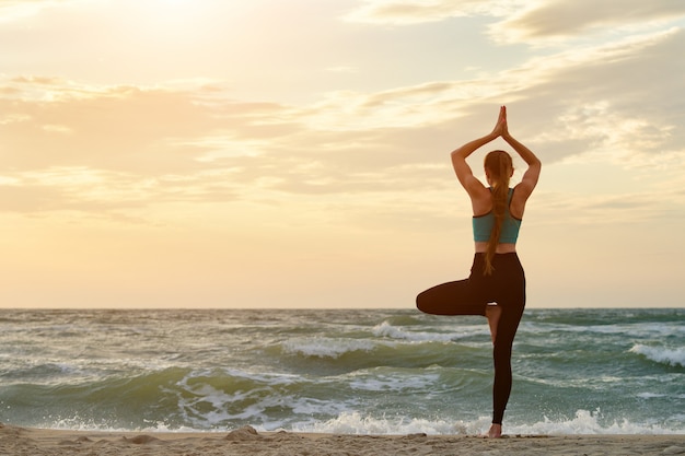 Mädchen auf übendem Yoga des Seestrandes. Rückansicht. Wunderschönes Sonnenlicht